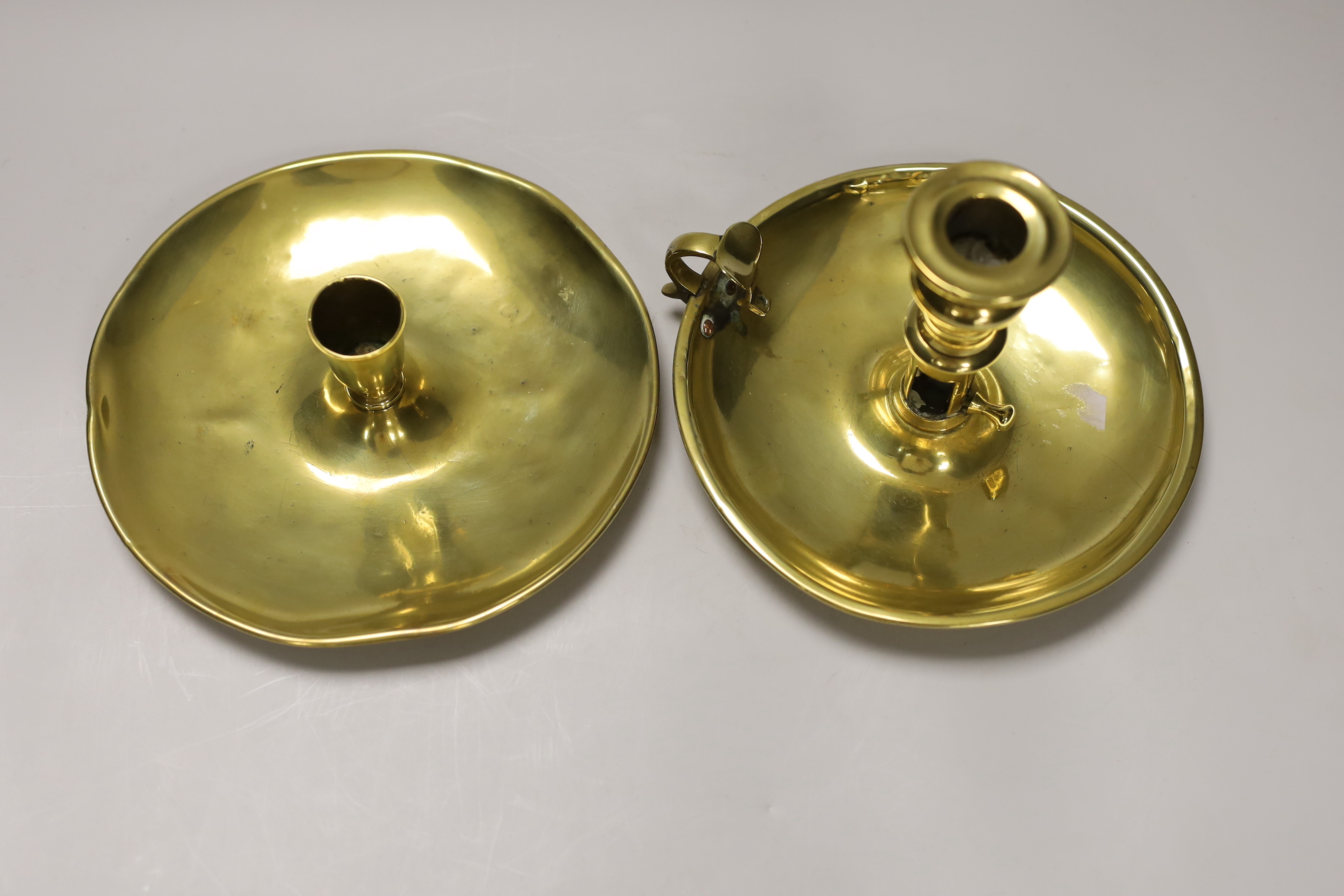 An 18th / 19th century brass saucer candlestick and an 18th century brass chamber candlestick, on circular tray